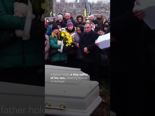 A father gently rocks the small coffin of his one-year-old son.